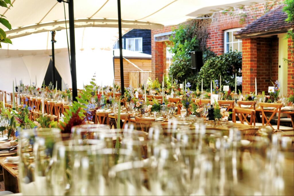 A beautifully decorated outdoor event setup featuring wooden tables, floral centerpieces, and elegant dinnerware under a tented canopy, showcasing how party rentals in Houston can transform a space for a stress-free and memorable event.