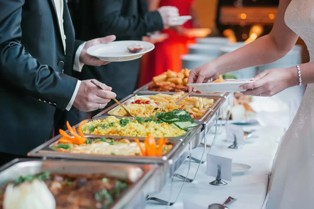 A wedding couple joyfully serves food to their guests at a beautifully decorated reception table.