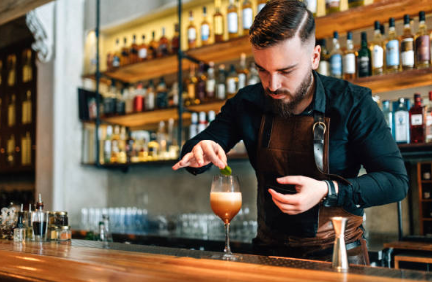 A bartender preparing a cocktail at a bar, focused on mixing ingredients with a shaker in a vibrant atmosphere.