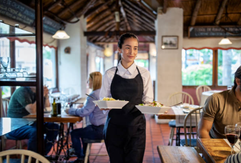 Waitress serving plated dishes in a rustic-style dining space with warm lighting, wooden tables, and cozy ambiance — ideal visual for Houston Party Rental Services showcasing professional staffing, on-site service, and elegant event setups tailored for weddings, fundraisers, and private parties.