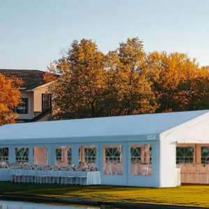 Large 20x70 white outdoor event tent with peaked roof and arched window panels, set up on grass near water. Interior features rows of tables and chairs for a formal gathering.
